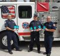 Three firefighters hold DETERRA Kits in front of the Newberry Fire Engine
