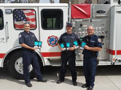 Three firefighters hold DETERRA Kits in front of the Newberry Fire Engine